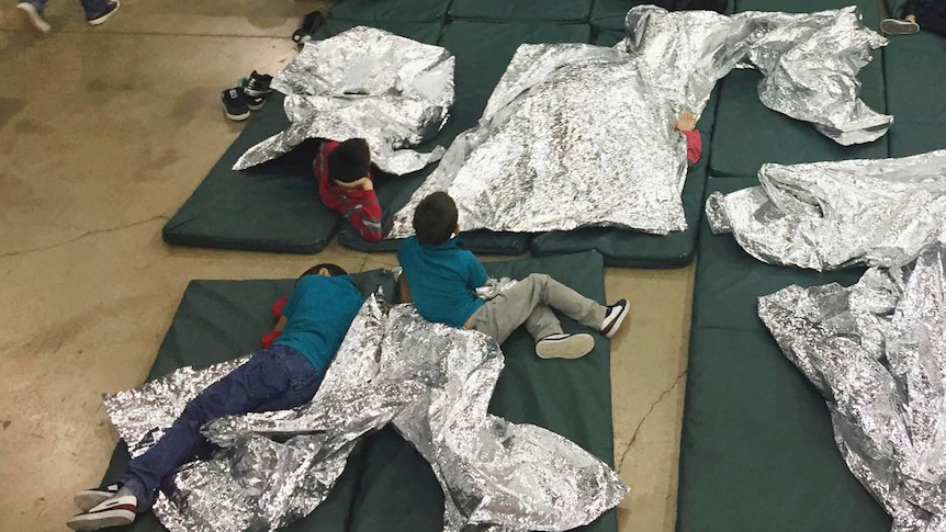 Kids lie on thin mattresses using large foil sheets as blankets.
