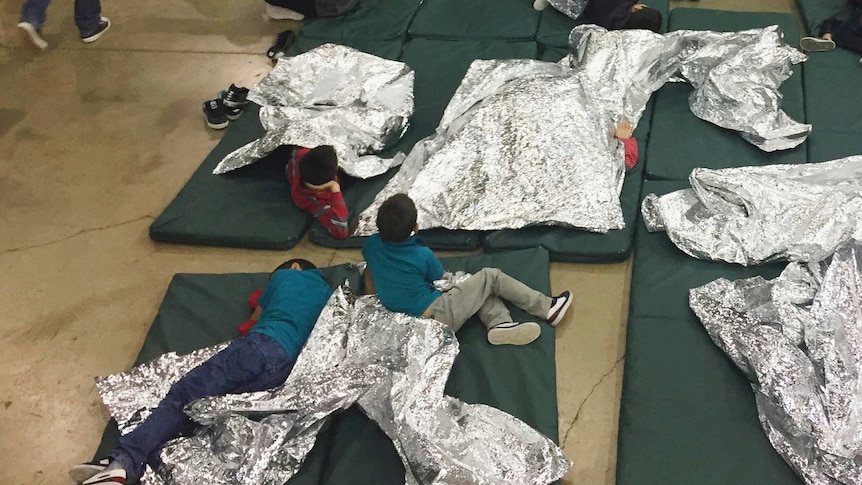 Children with silver blankets lie on mattresses on the floor.