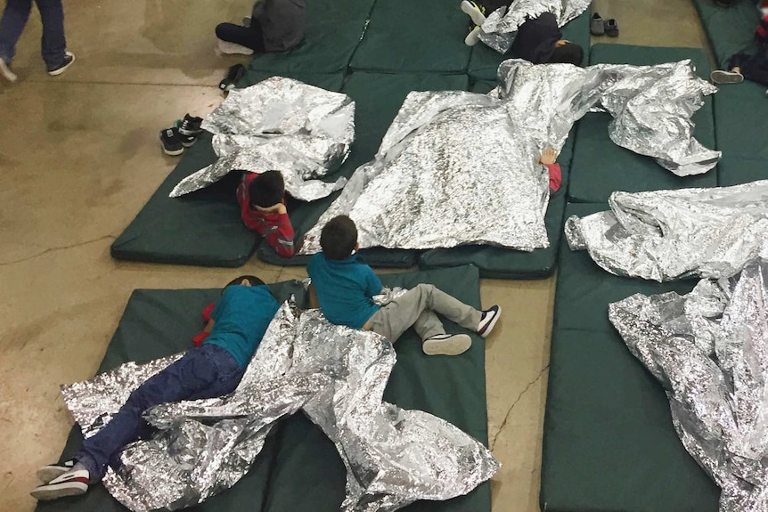 Kids lie on thin mattresses using large foil sheets as blankets.