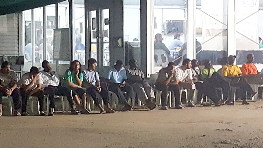 Asylum seekers sit and wait for food in a long queue in a Manus Island detention centre.