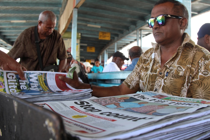 Two men look at the covers of Fijian newspapers.