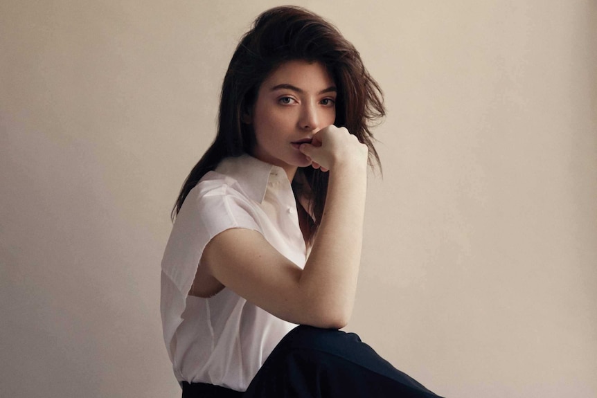 Lorde sitting on a stool and chewing on her thumb.