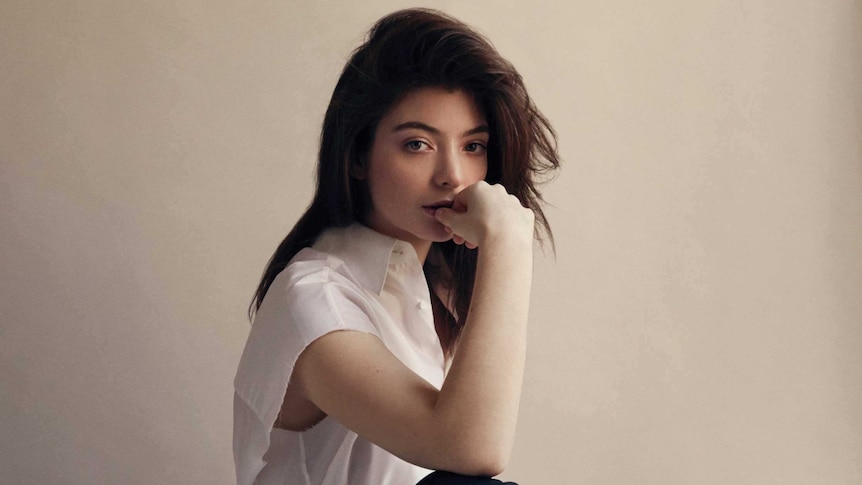 Lorde sitting on a stool and chewing on her thumb.