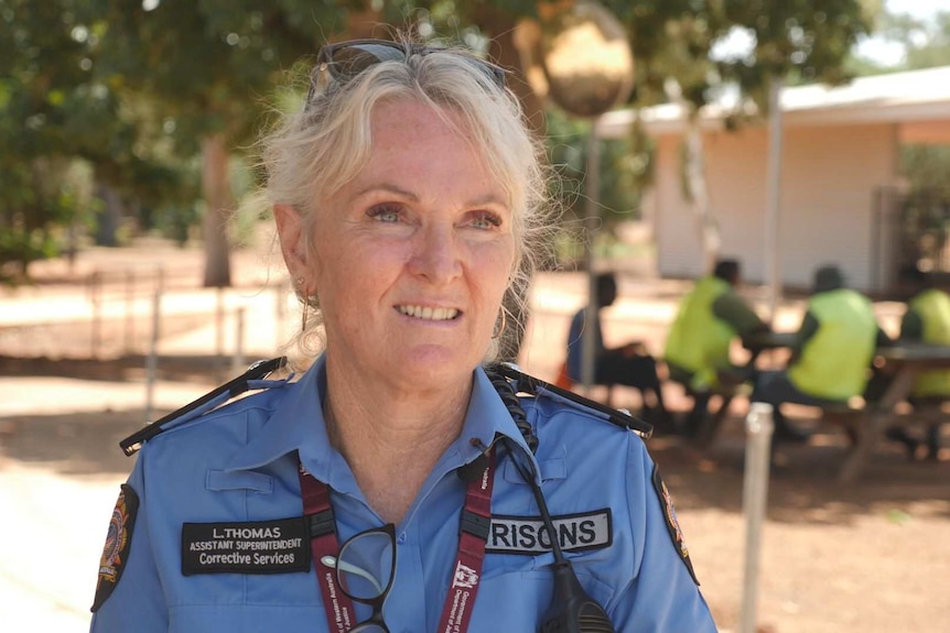 a woman in uniform with prisoners sitting at a table in the background.