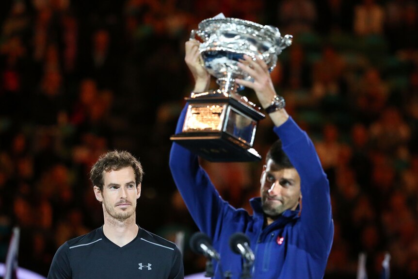 Andy Murray looks from behind at Novak Djokovic who is lifting a large silver trophy