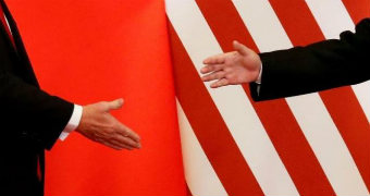 Donald Trump and Xi Jinping shake hands in front of two flags.