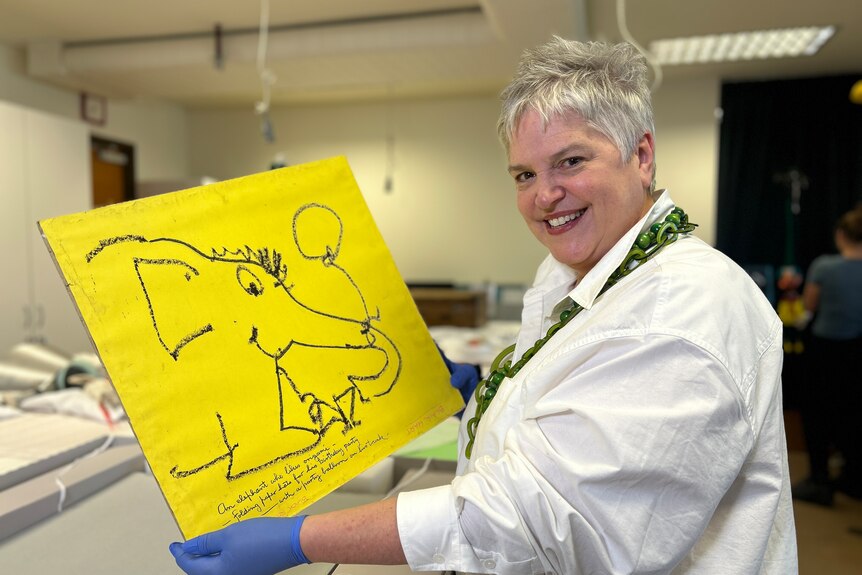 A woman holding a yellow piece of paper with a drawing on