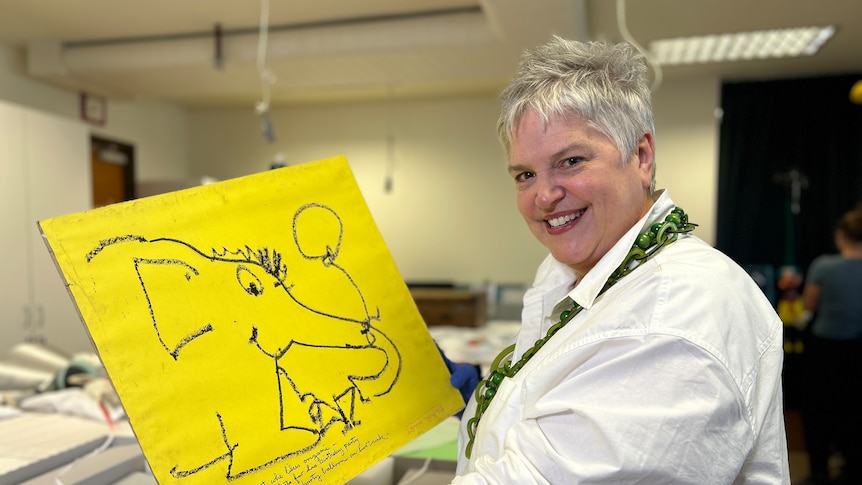 A woman holding a yellow piece of paper with a drawing on