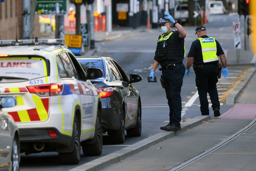 Victorian Police officers speak to a person in a car at a Police checkpoint.