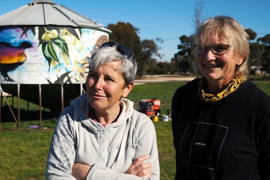 Two women standing in front of a painted silo.