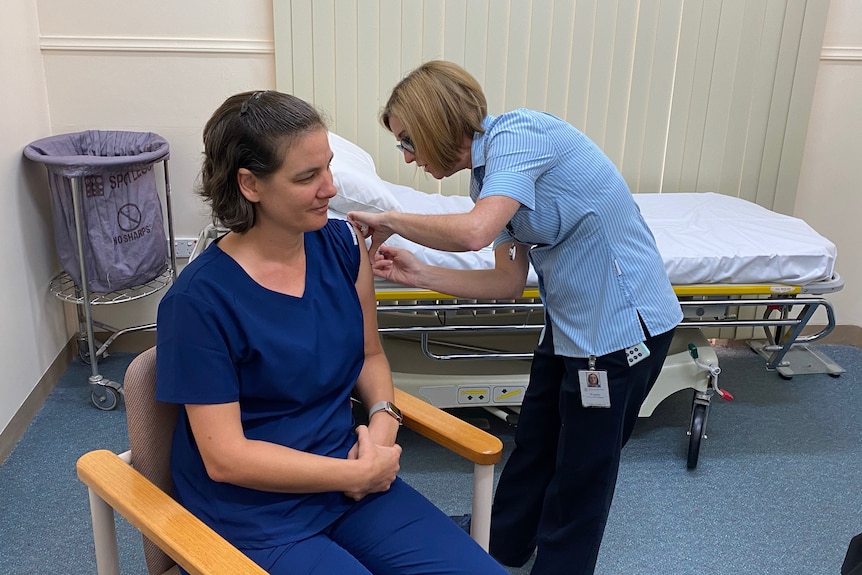 A doctor receives a vaccination from a nurse in a hospital room. 