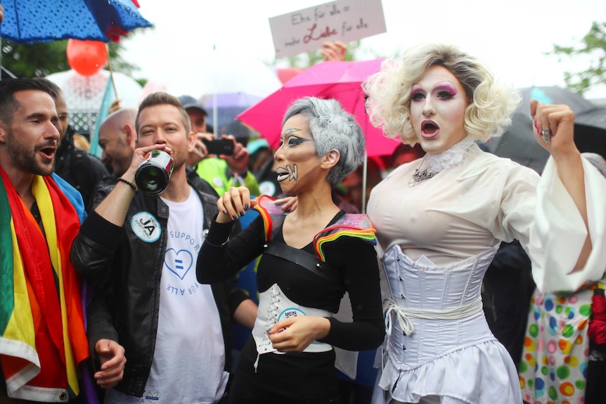 People dressed in drag attire drink champagne and celebrate in the street in Bundestag