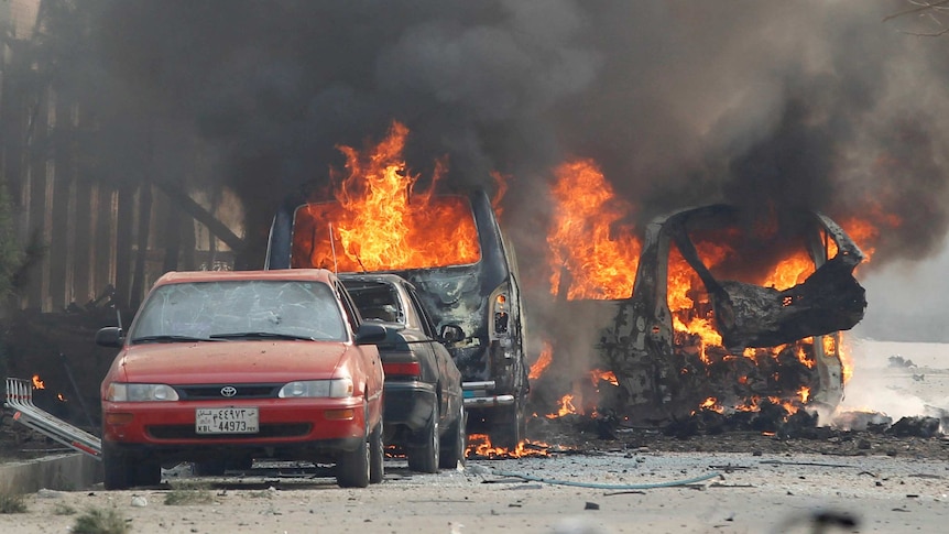 Long distance shot of several cars burning on a street.