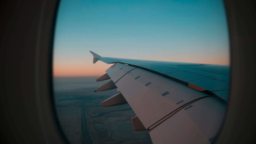 From inside a plane, you look out a window viewing the wing and the sky at dusk. 