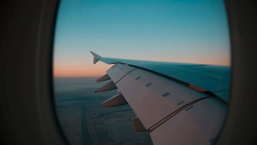 You look out of a plane window, viewing the rear of a wing and a sky at dusk.