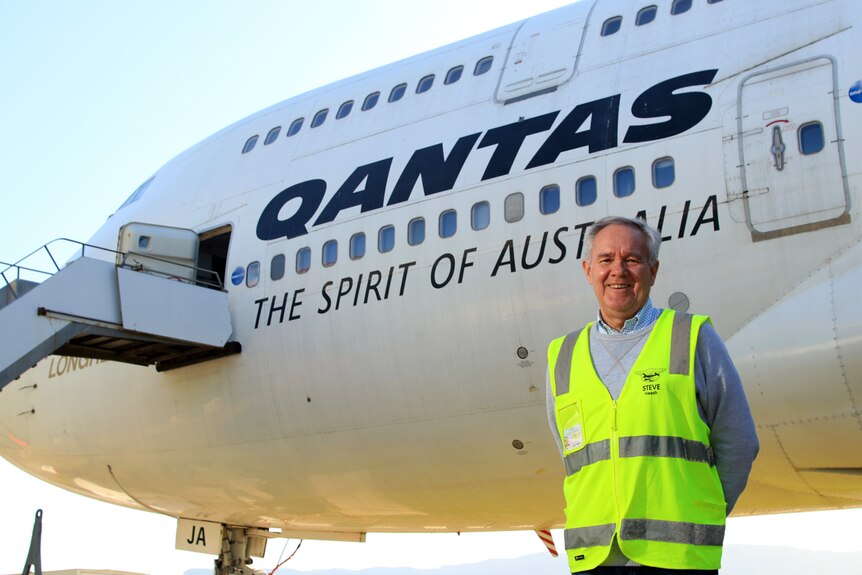 Steve Heesh stands in front of the Qantas 747 at Albion Park wearing a fluoro yellow vest.