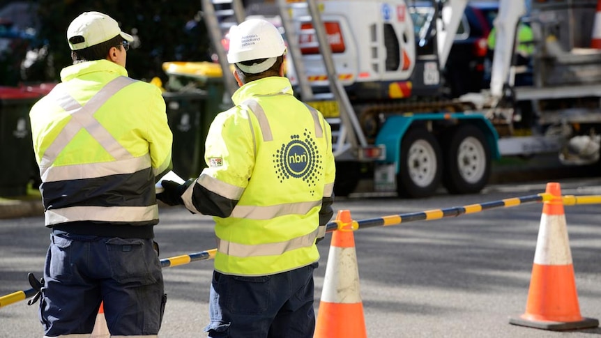 Two NBN workers in hard hats and fluorescent jackets' watch over construction.