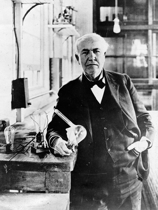 Black and white photo of Thomas Edison holding a light globe in a workshop