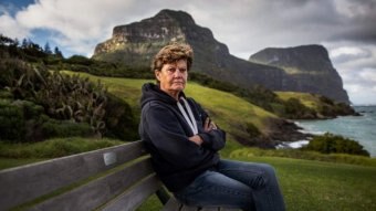 A woman sits on a park bench overlooking the ocean.