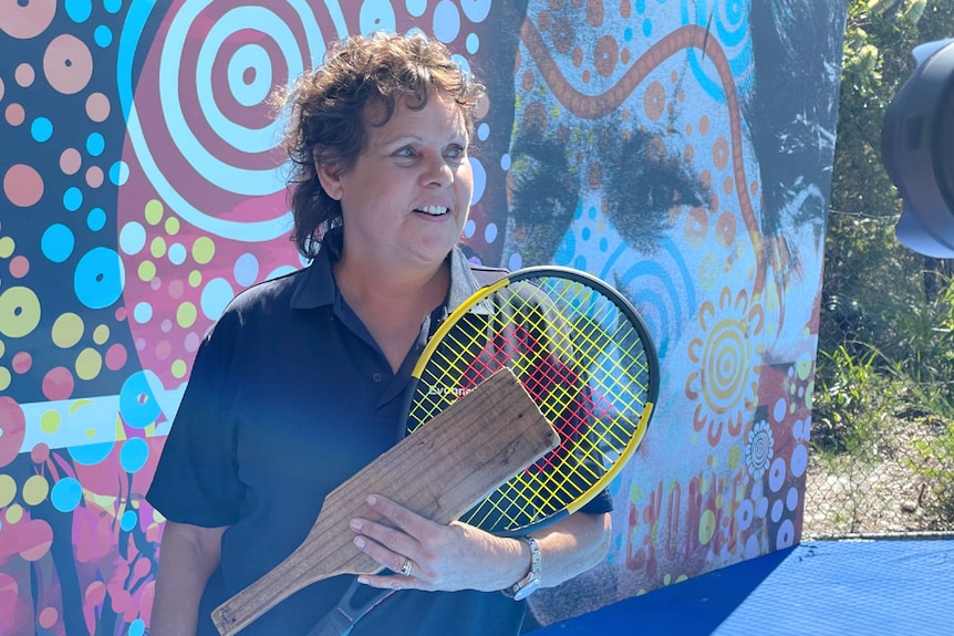 Woman holding tennis racquet in front of large mural with woman's face