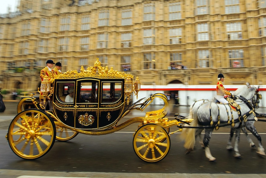 The queen inside a gold and black coach passes by parliament house