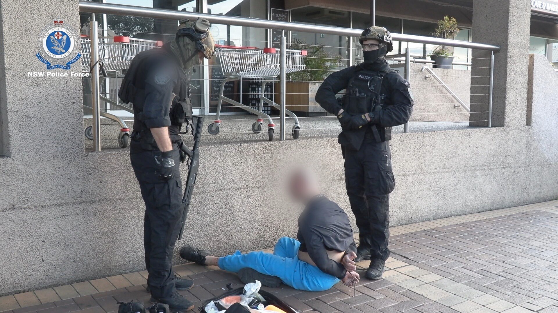 two police stand over a man with a blurred face sitting on the ground