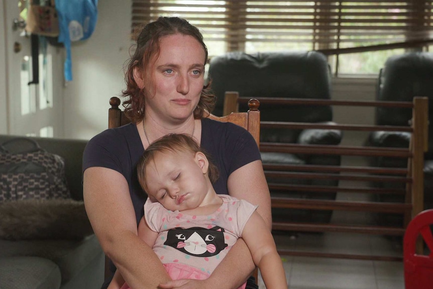 Bianca Hackett sitting on a chair holding her sleeping daughter in her lap