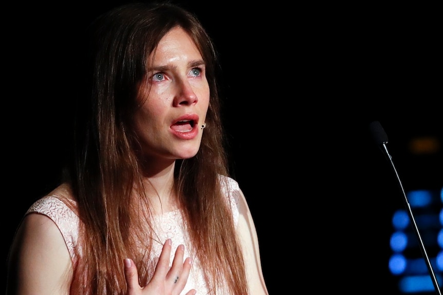 A woman looks upwards and holds her right hand over her chest as she becomes emotional while delivering a speech.