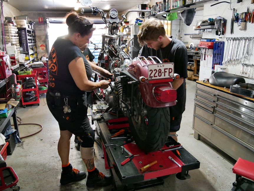 Три человека работают на мотоцикле в мастерской.