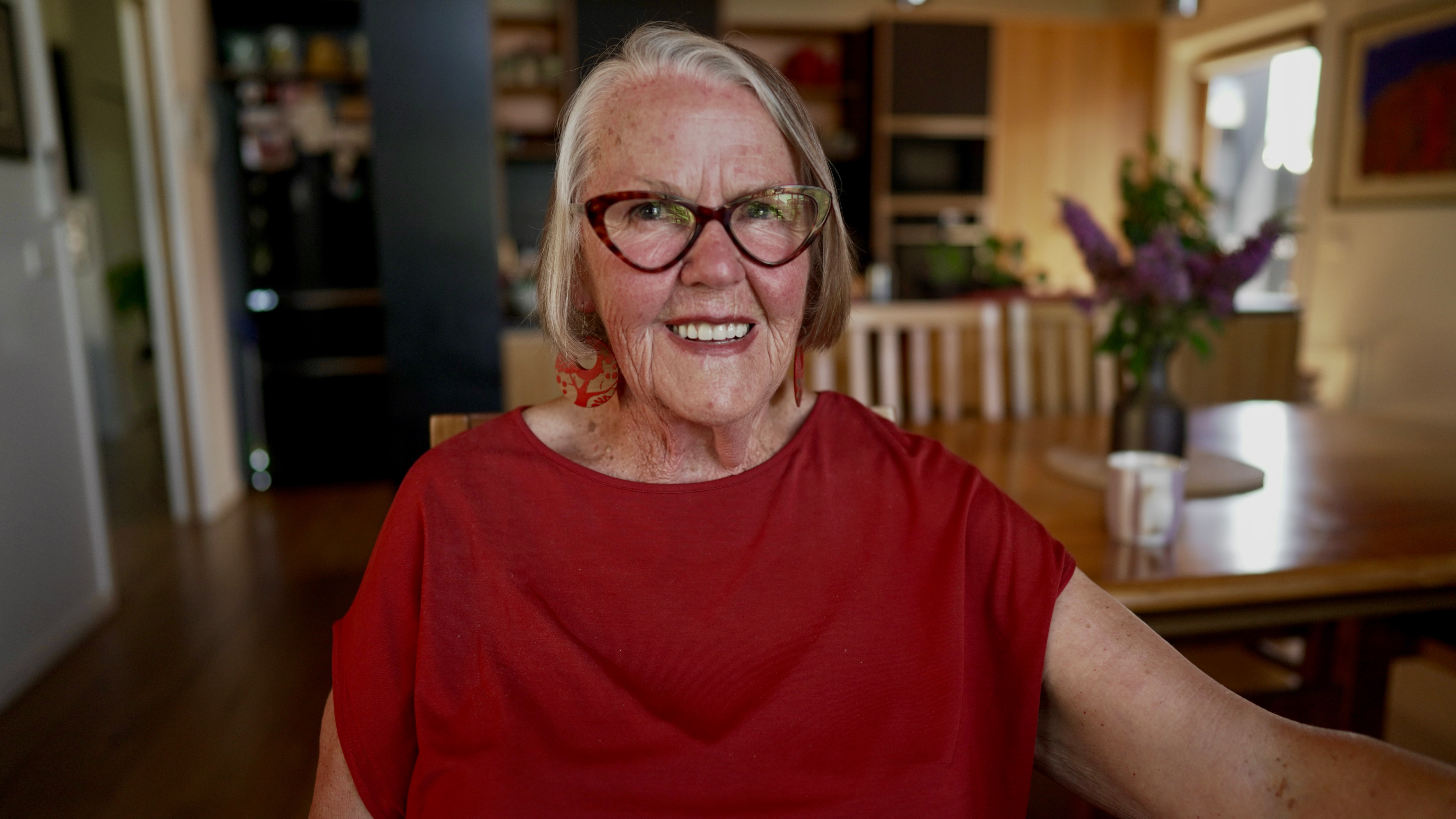 Older woman in a red shirt sitting in a dining room.