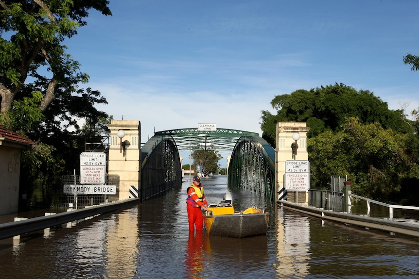 An SES volunteer walks a small boat through the floodwaters at the Kennedy Bridge in Bundaberg. 