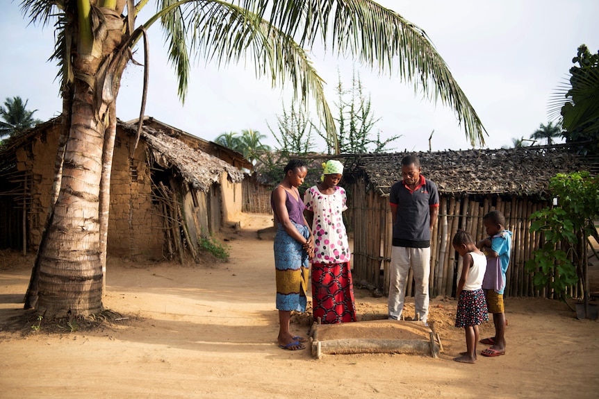 a family stands around the grave of a small child in a village in the Democratic Republic of Congo