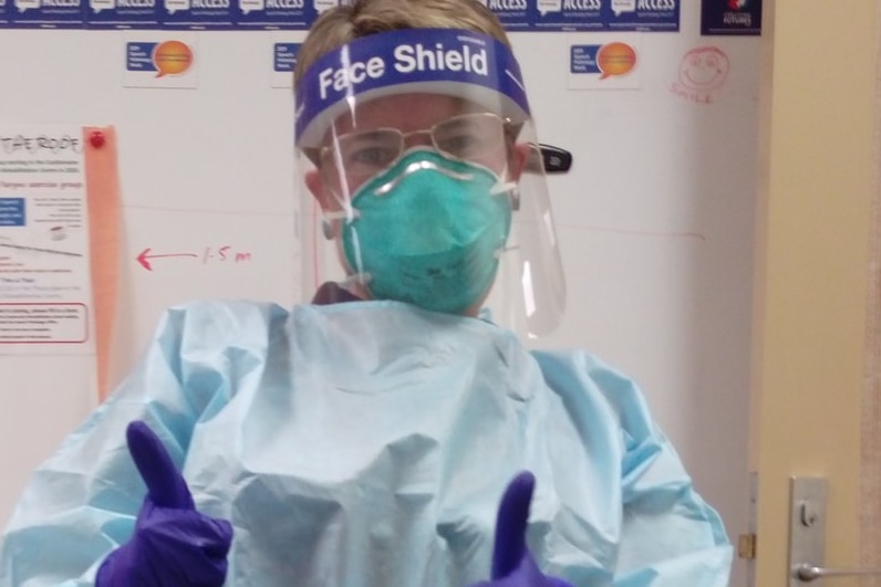 woman wearing PPE including mask and face shield gives a thumbs up.