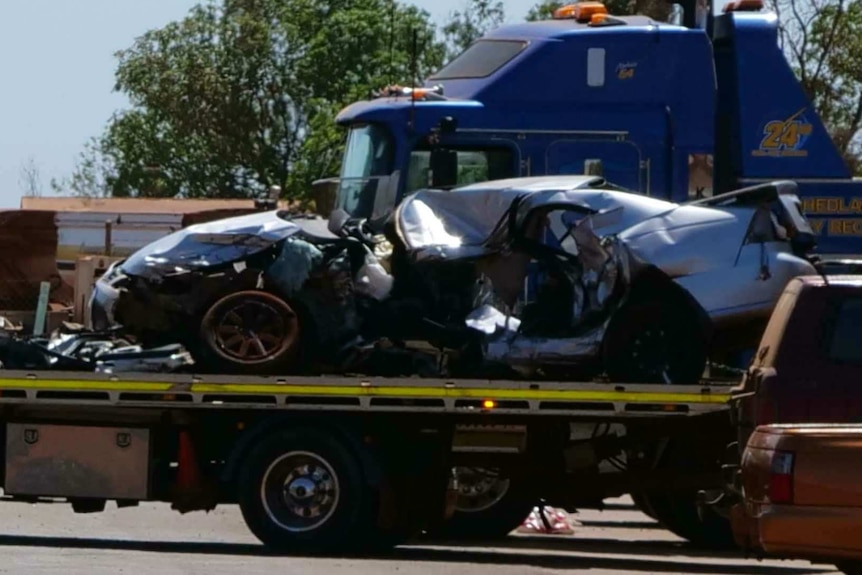 A crushed silver car sits on the back of a tow truck.