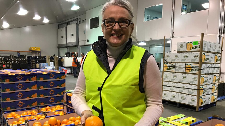 Sue Middleton holds two oranges in a warehouse while smiling.