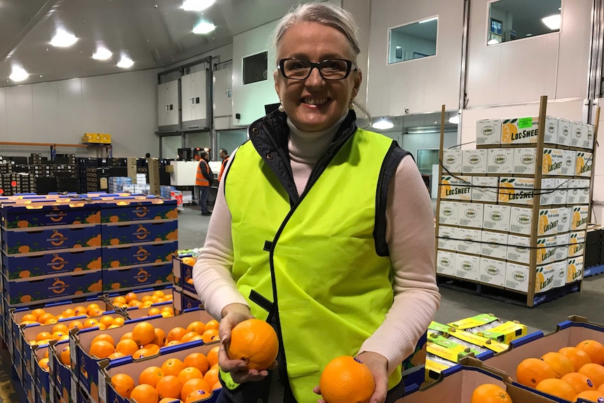 Sue Middleton holds two oranges in a warehouse while smiling.