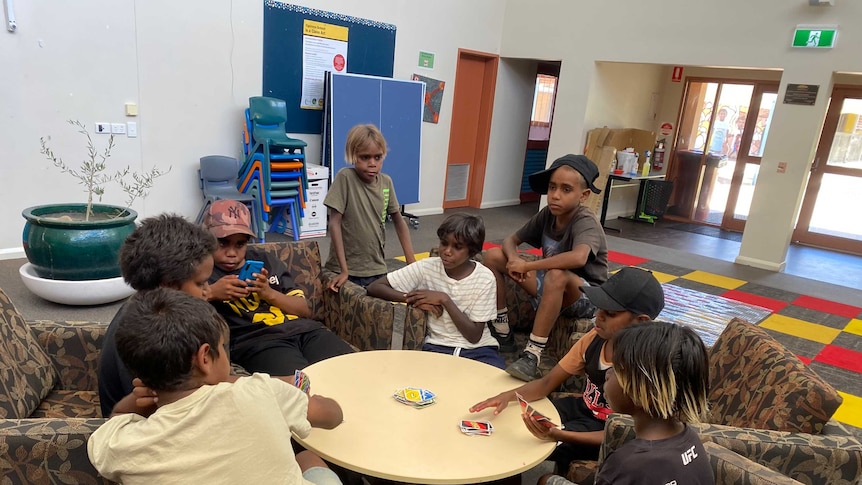 Eight young boys sit around a circular table indoors playing the card game Uno.