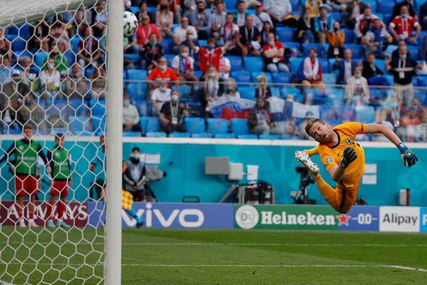 A goalkeeper twists in mid-air as he watches the ball fly past him into the top corner during a Euro 2020 game.