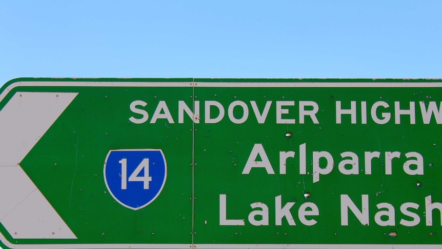 A picture of a road sign indicating the direction of the Sandover highway. It has bullet holes in it.