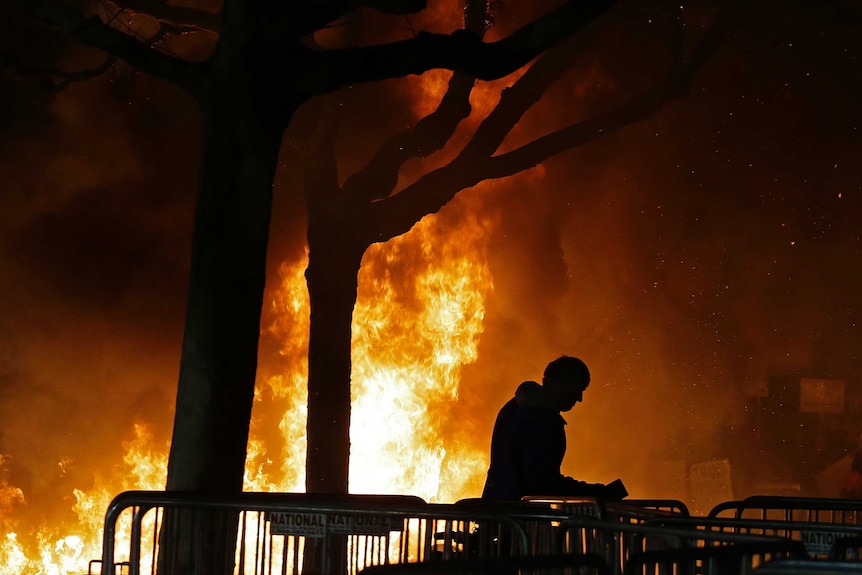 A bonfire blazes with a person in front of it.