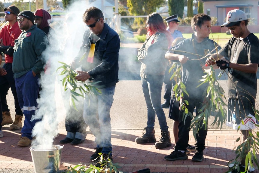 A man puts gum leaves into a silver bucket for an Indigenous smoking ceremony.