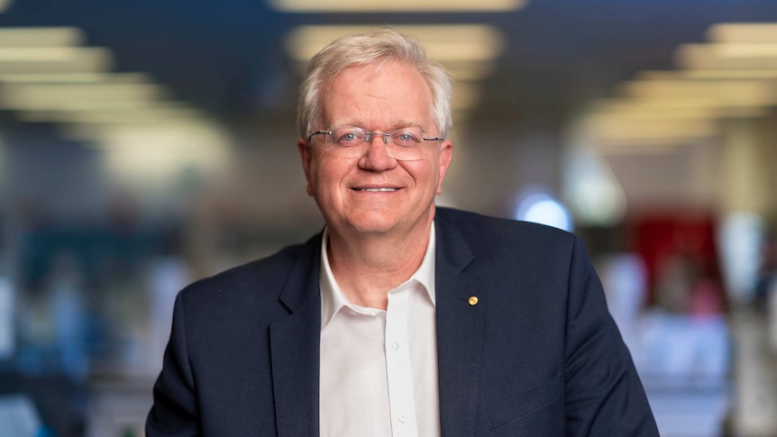 Brian Schmidt wearing a black jacket and smiling for the camera in front of some trees.