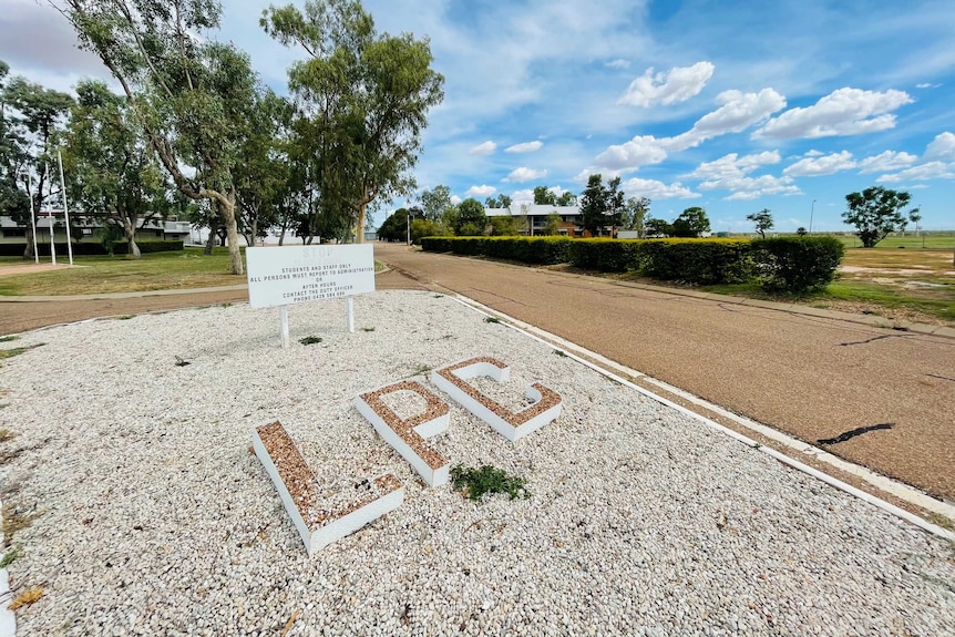 Large letters LPC on gravel beside a road lined with shrubs.