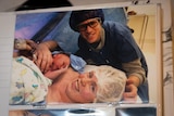A picture in a scrapbook of parents in hospital hugging an infant child.