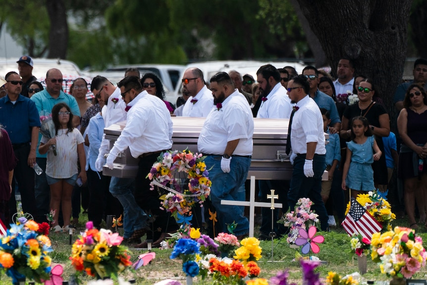 Pallbearers carry a coffin with flowers in the foreground