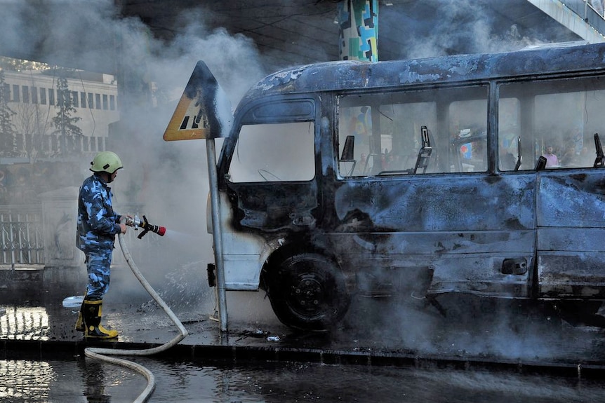 A civil defense member hoses down a bus that is burned out and charred after being bombed 