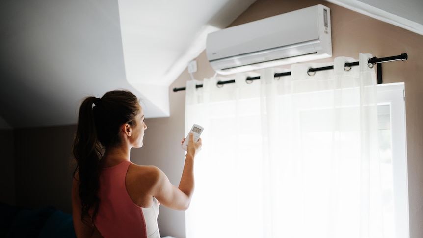 Woman in active wear using a remote control for air conditioner in a loft room.