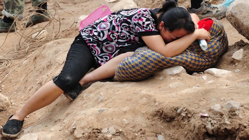 A woman cries while over the body of her child amid the rubble of landslide devastation