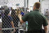A Border Patrol agent holds a gate open as kids walk out of a cage.
