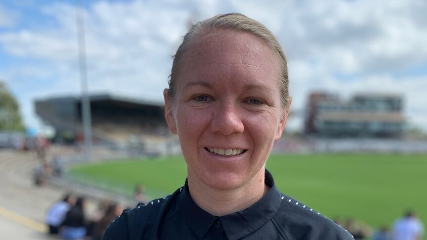 Aasta O'Connor wears a blue polo t-shirt and stands in front of a footy oval.